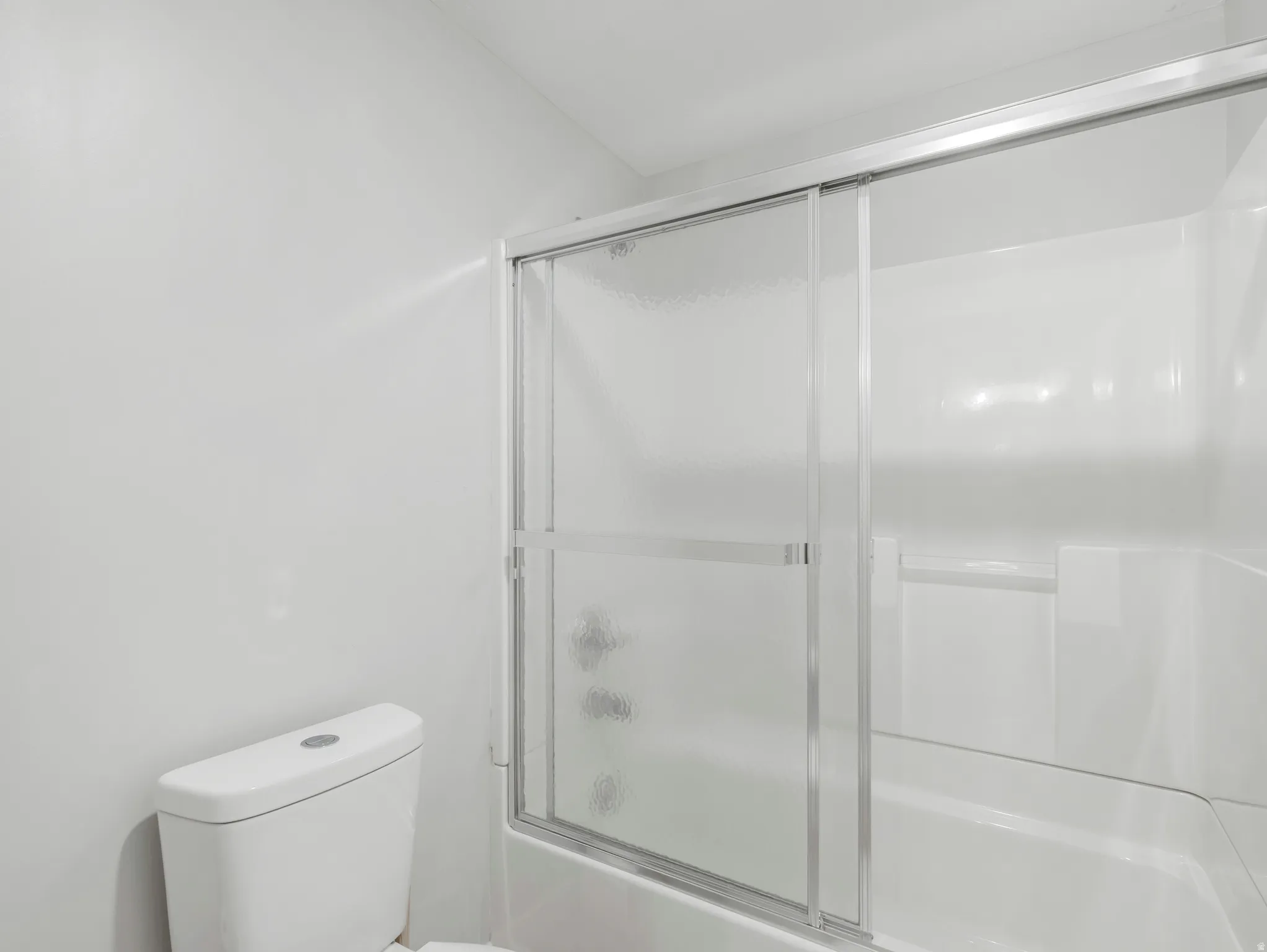 Bathtub shower combination with sliding glass enclosure and white toilet