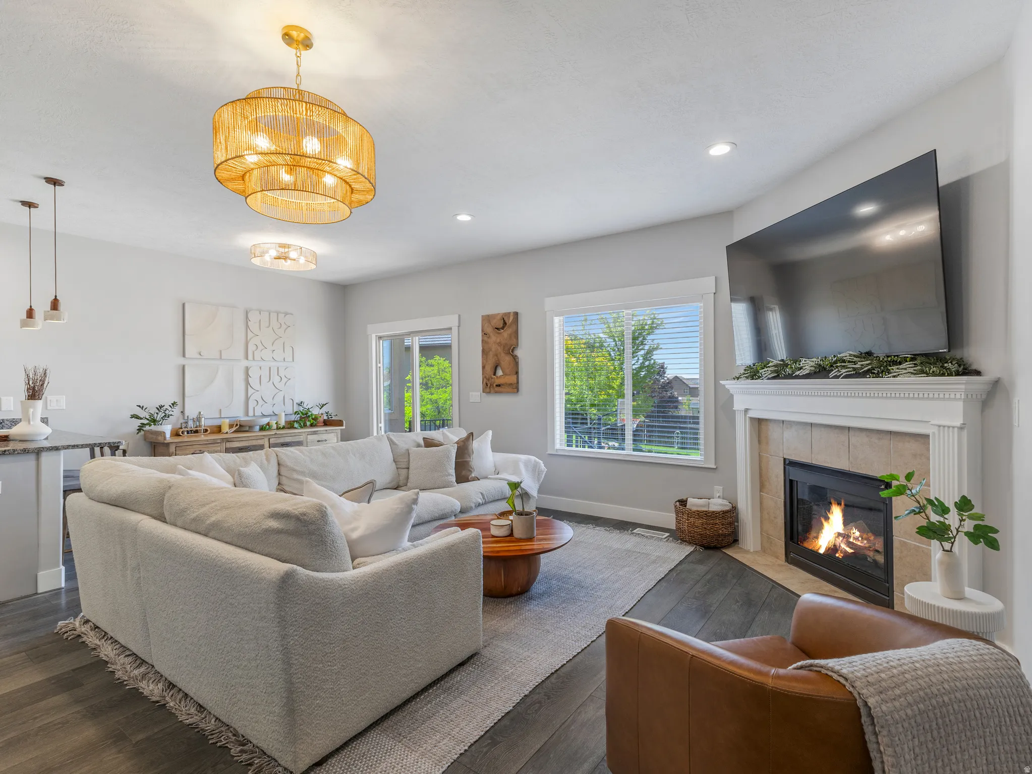 Living area featuring wood-finish flooring, a corner fireplace with a tiled surround and white mantel, and multiple windows with blinds