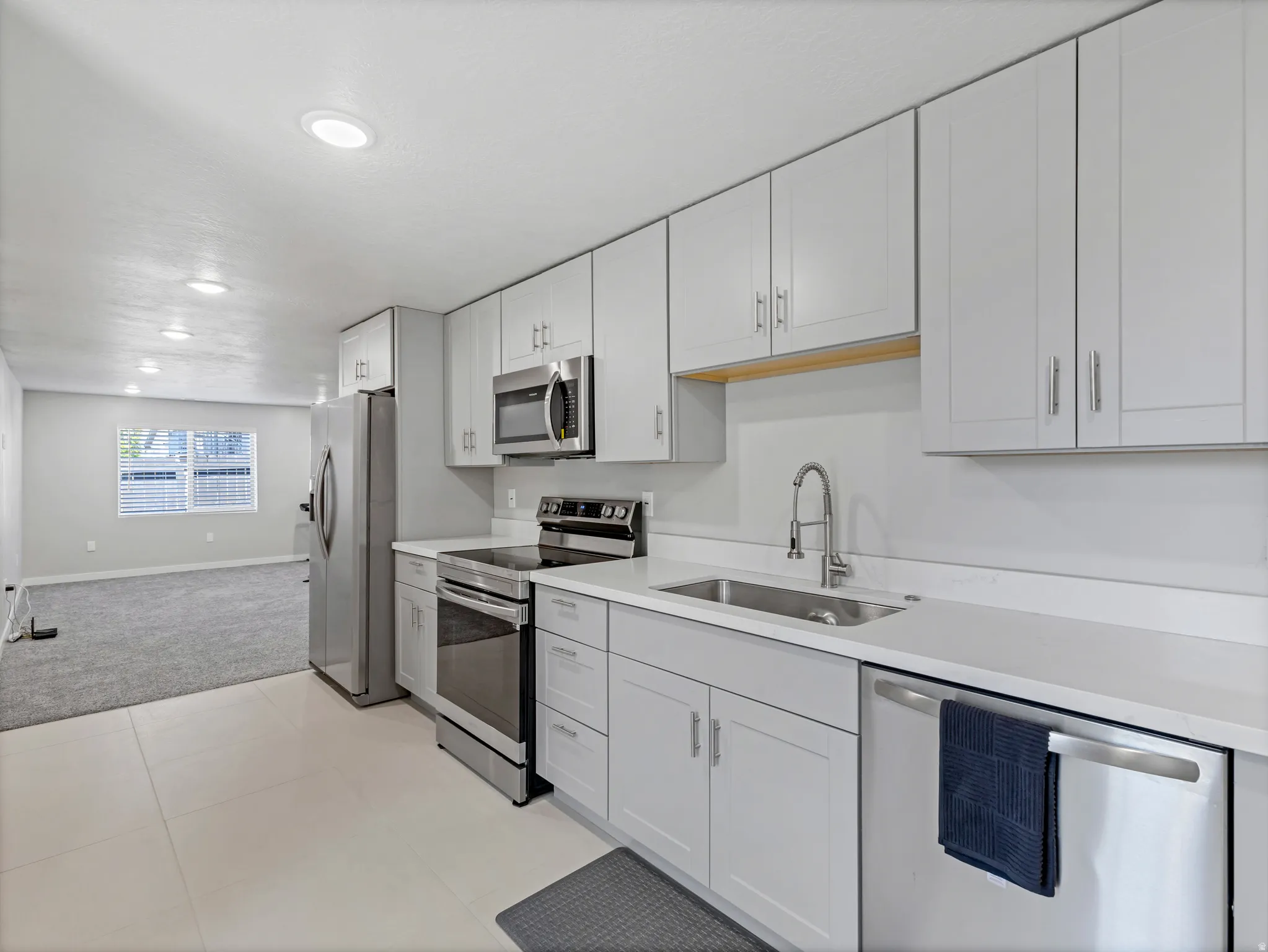 Modern kitchen featuring light gray cabinetry with brushed nickel hardware, stainless steel appliances, and white countertops