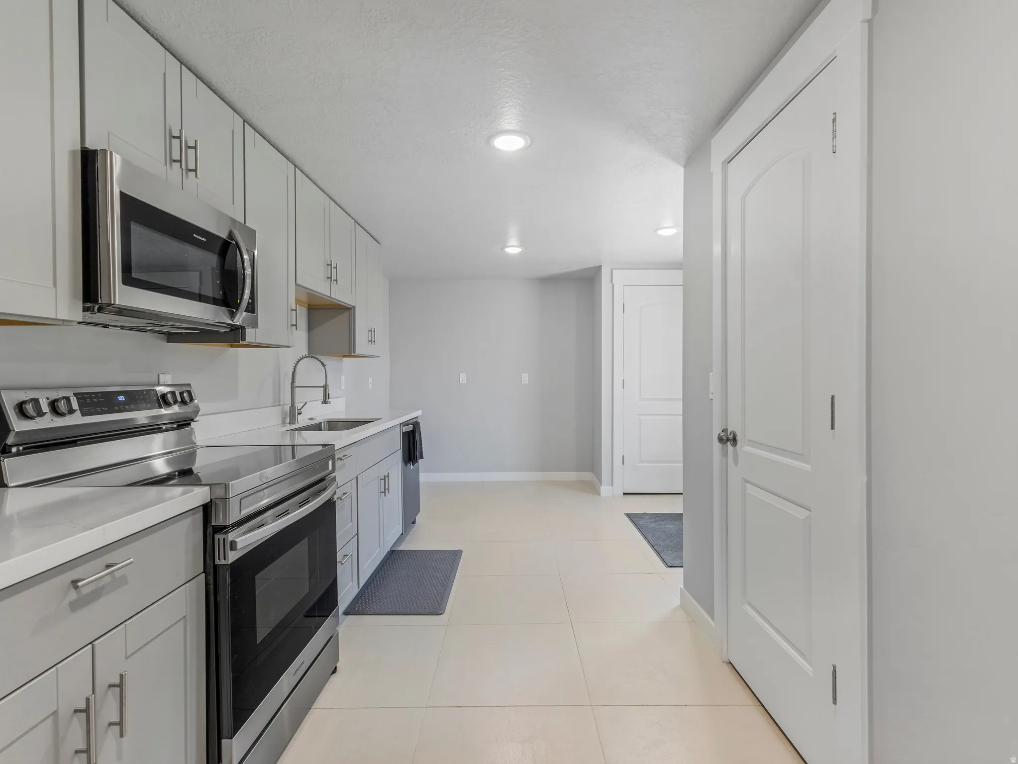 Modern kitchen featuring light gray cabinetry, stainless steel appliances, white countertops, a stainless steel sink with a high-arch faucet, and recessed lighting