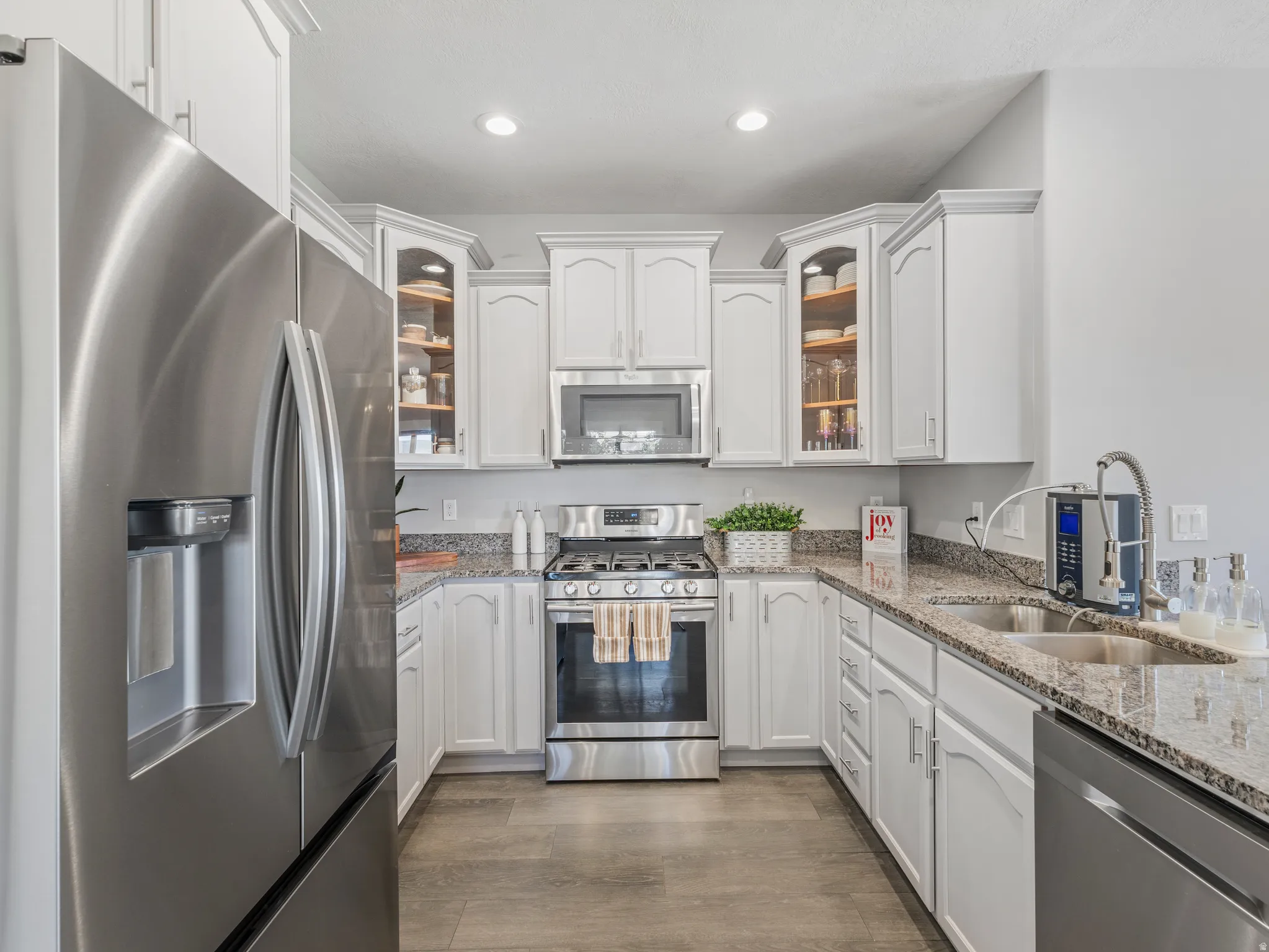 Contemporary kitchen featuring white cabinetry, stainless steel appliances, granite-style countertops, and wood-finish flooring
