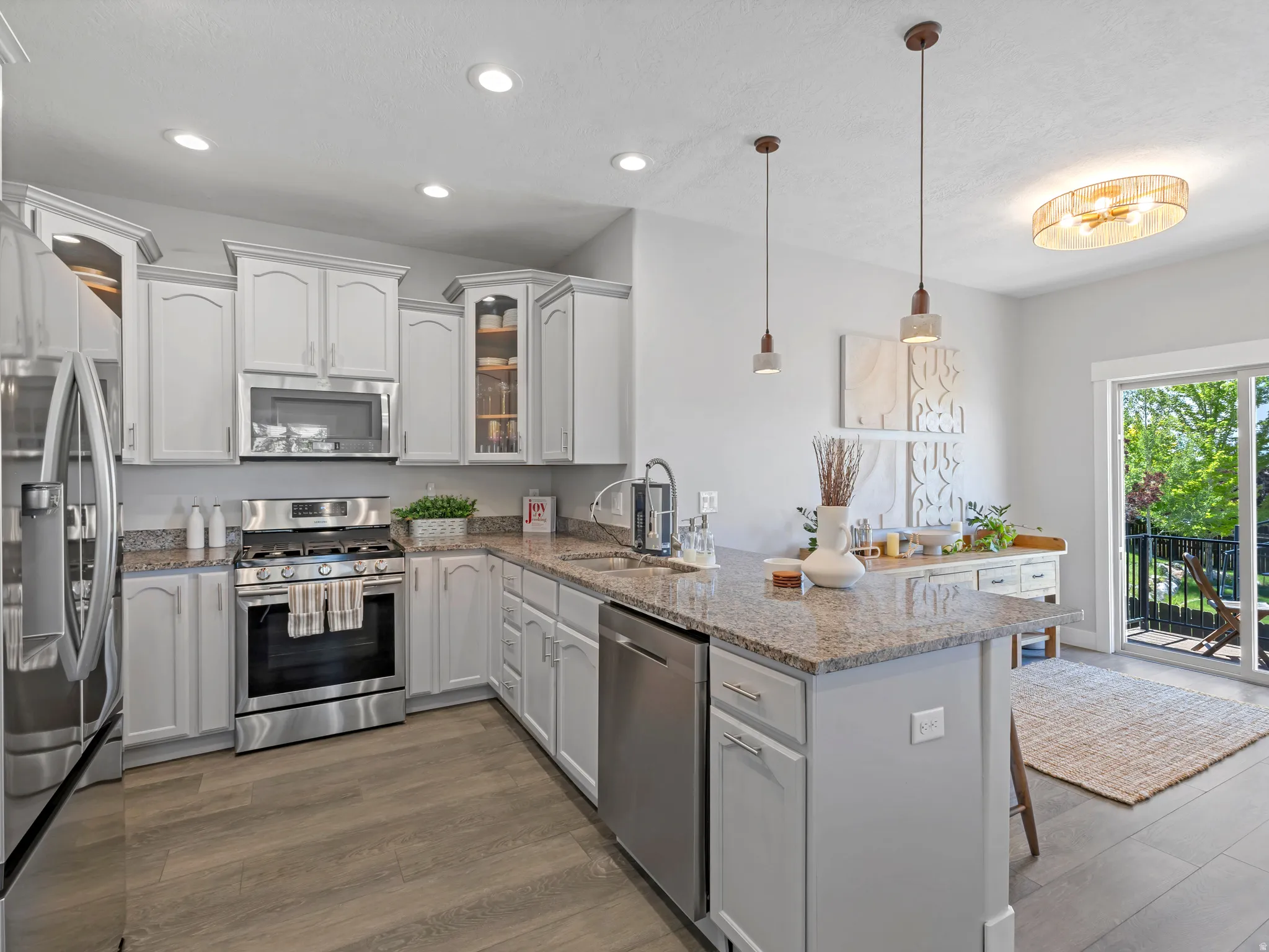 Kitchen featuring light-toned cabinetry, stainless steel appliances, speckled stone countertops, and wood-finish flooring
