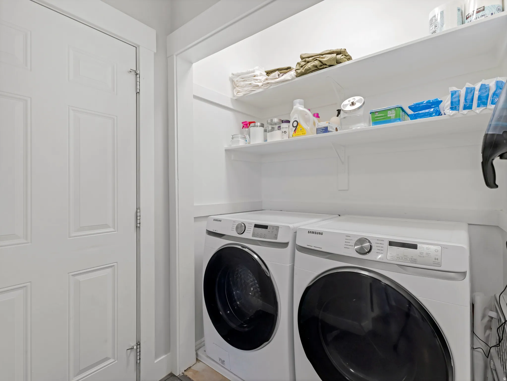 Dedicated laundry area featuring a white six-panel door, built-in shelving, and a white front-loading washer and dryer set