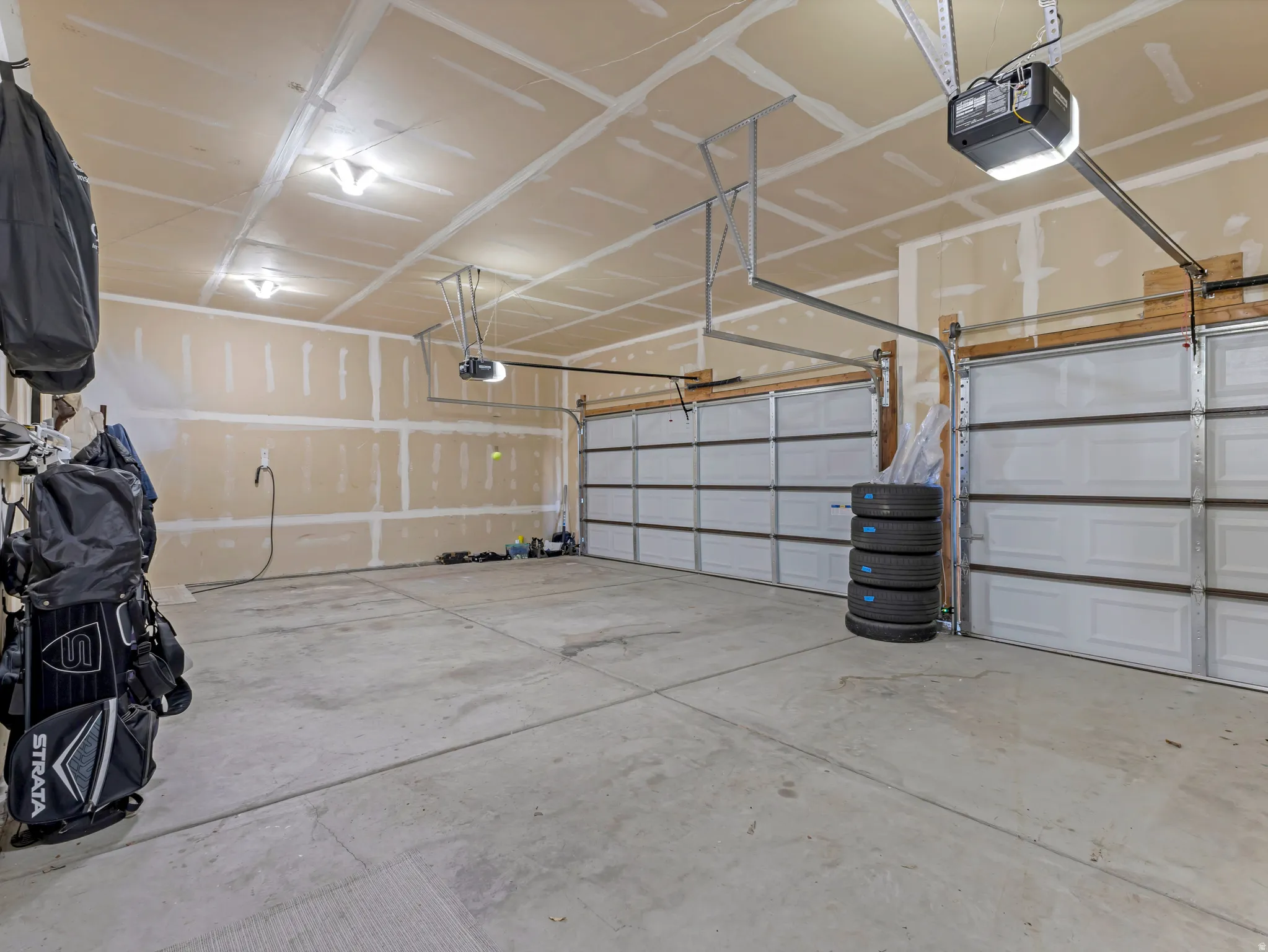 Spacious garage featuring two overhead doors, concrete flooring, exposed drywall, and overhead lighting fixtures