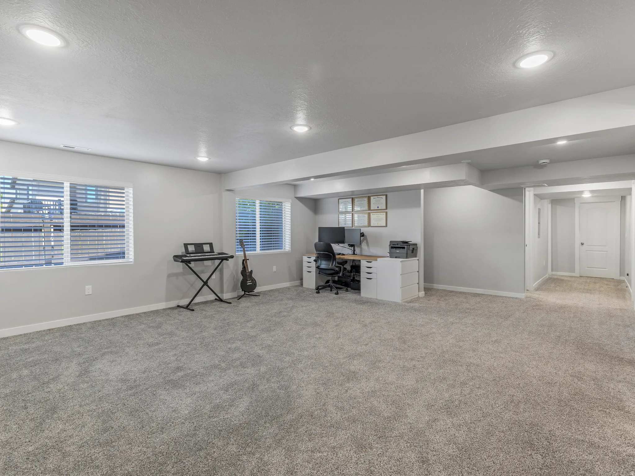 Expansive room featuring plush gray carpeting, recessed ceiling lighting, multiple windows with blinds, a built-in alcove, and neutral wall finishes