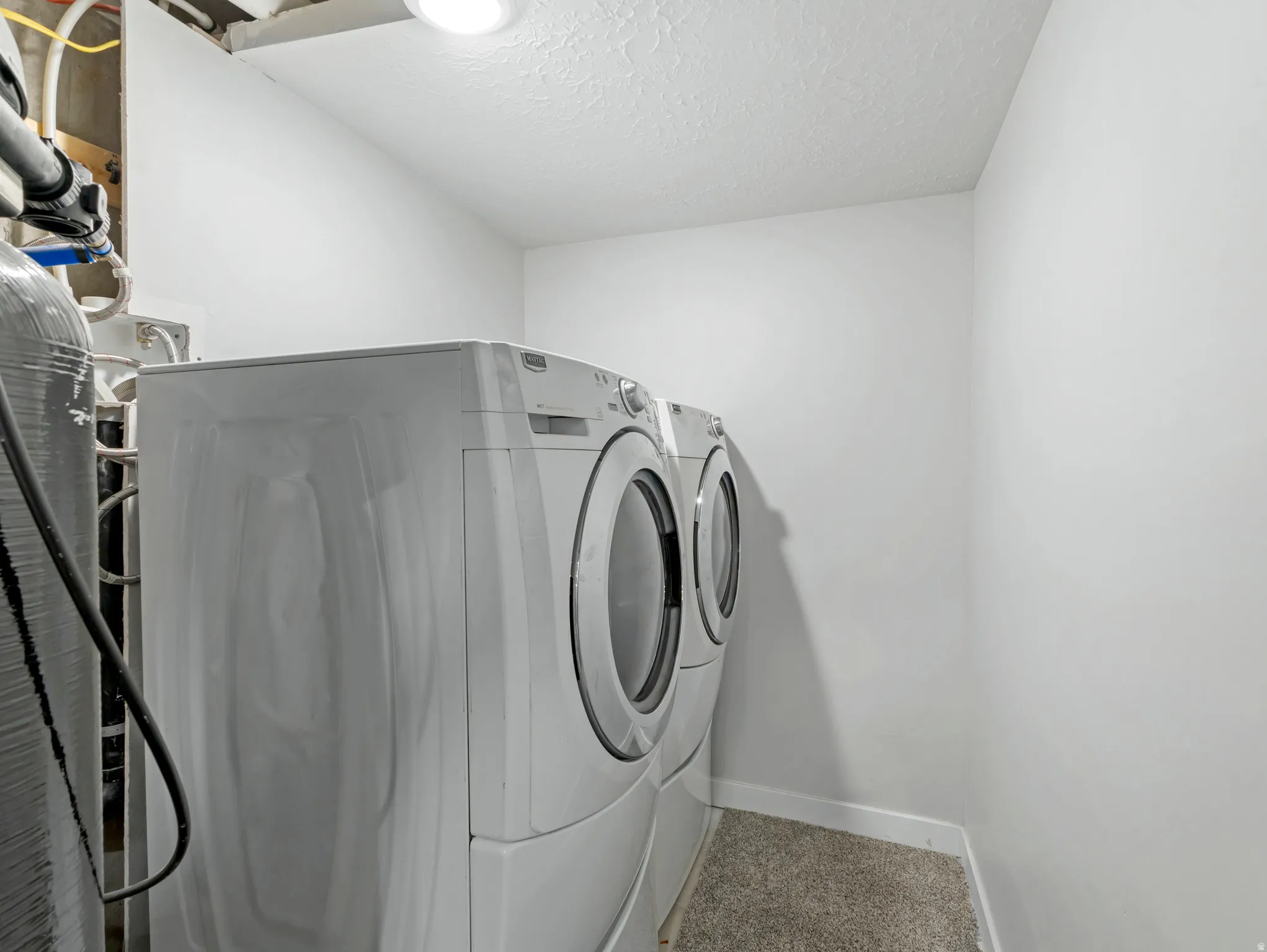 Dedicated laundry area featuring a front-loading washer and dryer, recessed ceiling lighting, light-colored walls, and a textured floor covering