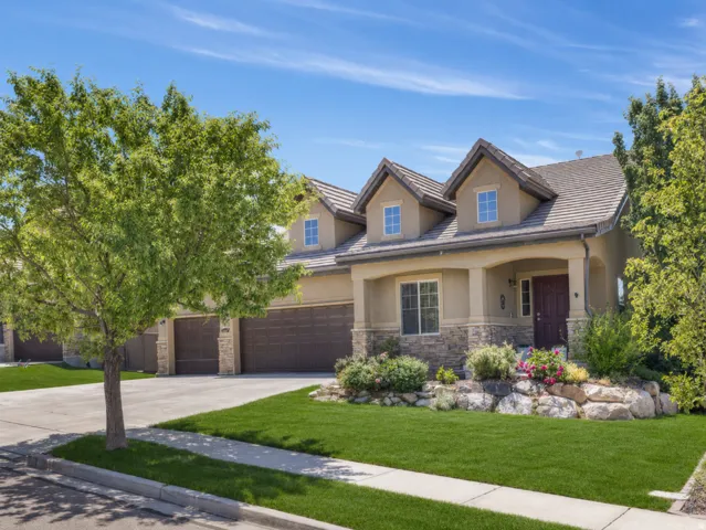Stucco and stone facade home featuring a covered entry porch, a multi-car garage with individual doors, and dormer windows