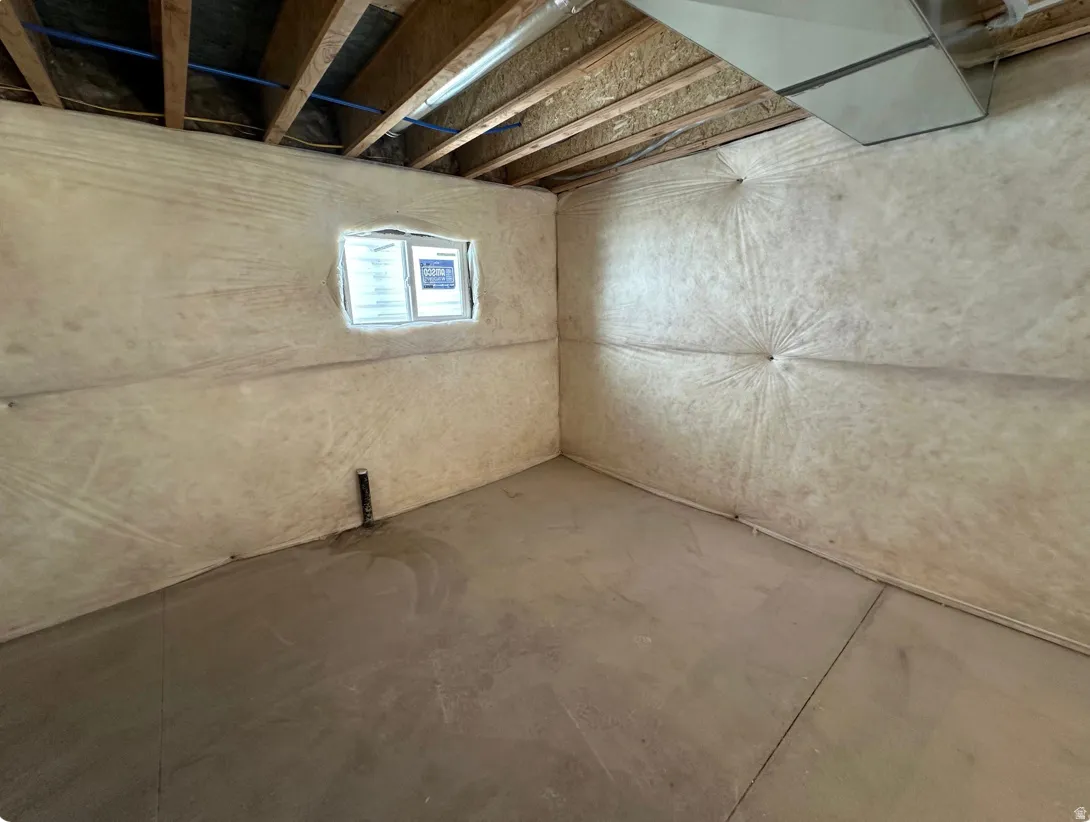 Unfinished basement space featuring exposed ceiling joists, insulation-wrapped walls, a small window, and a concrete floor
