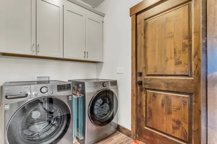 Utility area featuring light-toned upper cabinetry, wood-finish flooring, and a paneled wooden door with a matte black handle