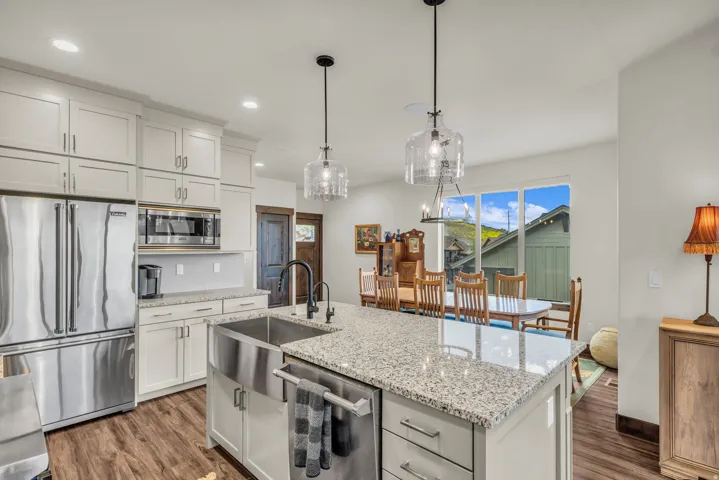 Modern kitchen featuring light-toned cabinetry, stainless steel appliances, wood-finish flooring, granite countertops, and a large farmhouse sink