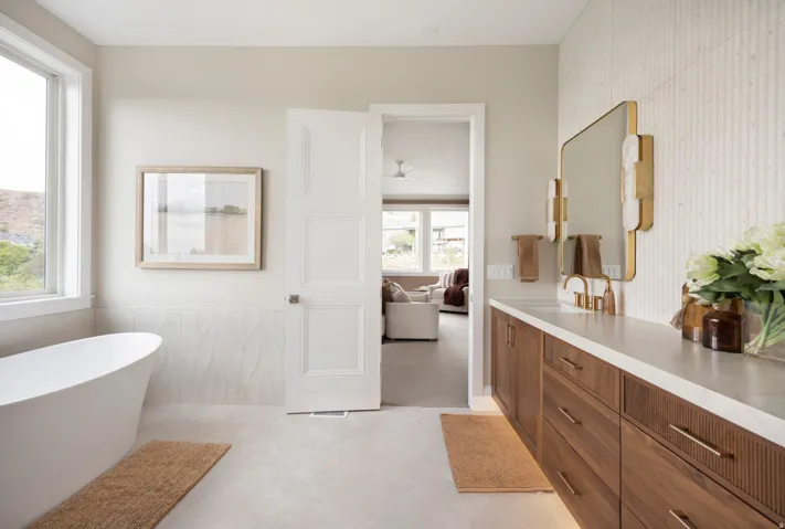 Bathroom featuring a freestanding soaking tub, large window, wood-finish vanity with a light-toned countertop, and vertical fluted wall tiling