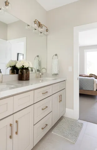 Double vanity featuring two integrated sinks, light-toned cabinetry with gold-finish hardware, and a substantial mirror