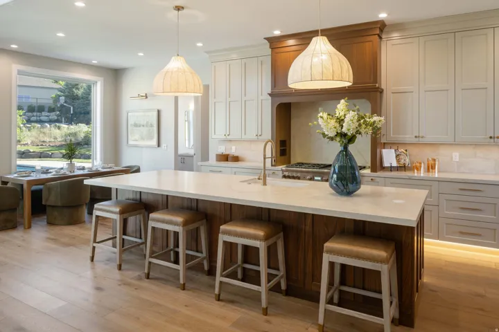 Spacious kitchen featuring a large central island with seating, pendant lighting, wood-finish flooring, light-toned cabinetry, and a built-in range hood
