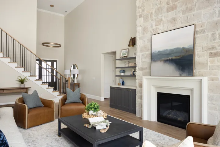 Spacious living area featuring a stone-clad fireplace with a classic mantel, built-in shelving, a grand staircase with dark metal railings, and soaring ceilings