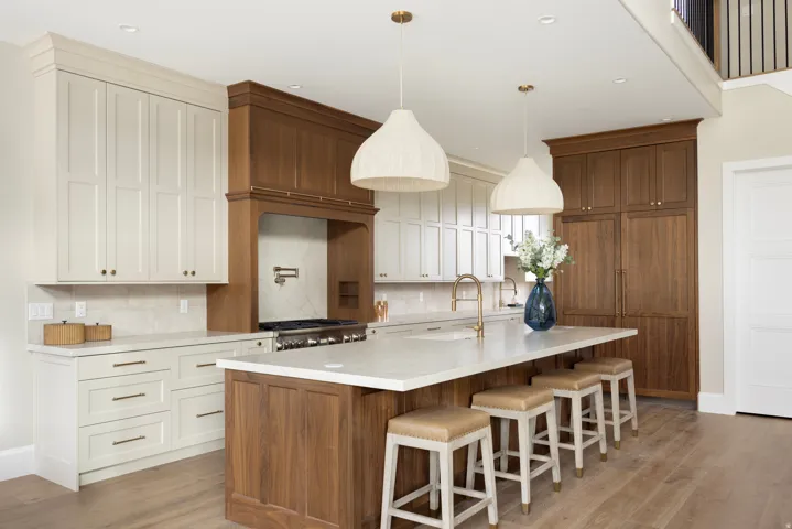 Gourmet kitchen featuring a substantial central island, two-tone cabinetry with integrated appliances, a professional range with a pot filler, and wood-finish flooring
