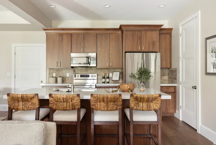 Kitchen featuring a central island with white countertop, wood-finish cabinetry, stainless steel appliances, and tile backsplash