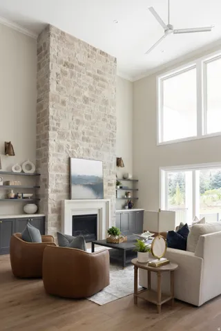Two-story living area featuring a floor-to-ceiling natural stone fireplace with a white mantel, wood-finish flooring, and high ceilings