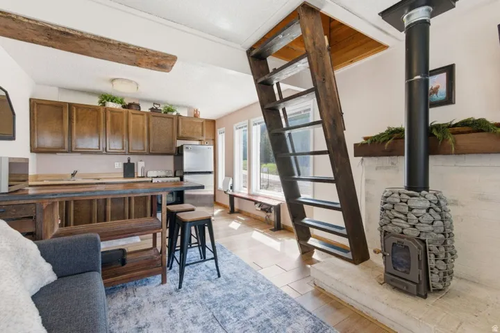 Living area featuring a stone-clad wood-burning stove with a black flue, a wooden ladder, and wood-finish flooring