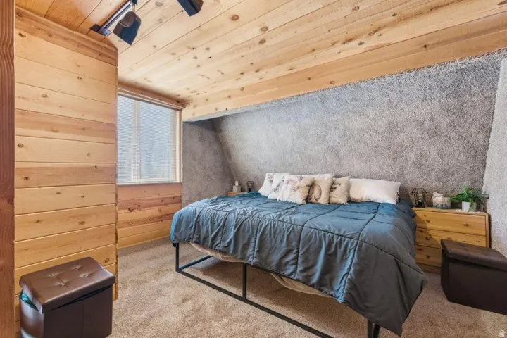 Bedroom featuring wood-paneled walls and ceiling, textured wall finish, and a window with blinds