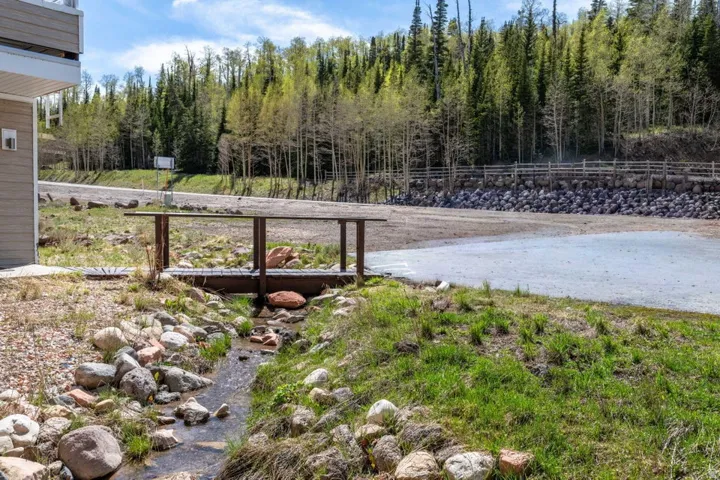 Wood bridge over a natural stream, with a gravel parking area and a forested backdrop