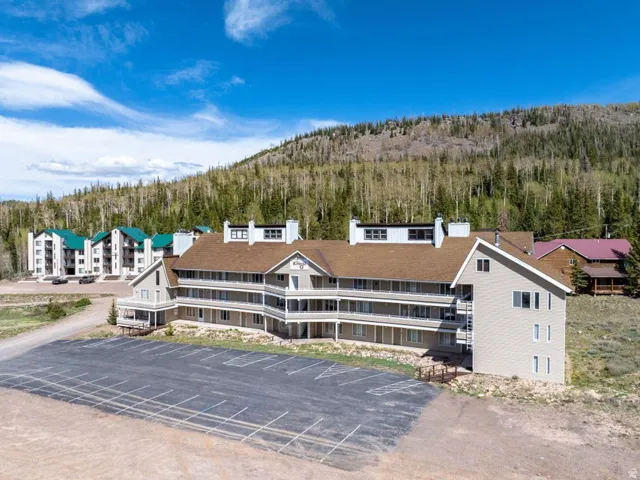 Multi-story building featuring a pitched shingle roof, multiple balconies, and a paved parking area