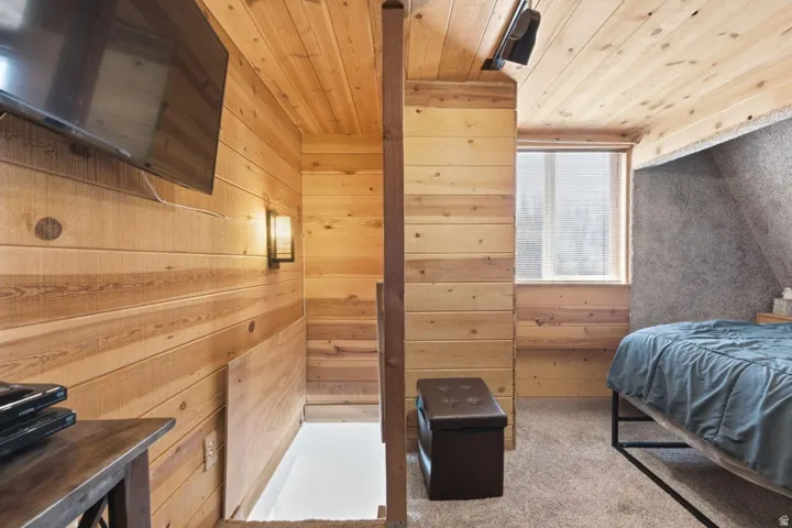 Wood-paneled room featuring a window with white blinds, wall-mounted television, and a built-in wall sconce
