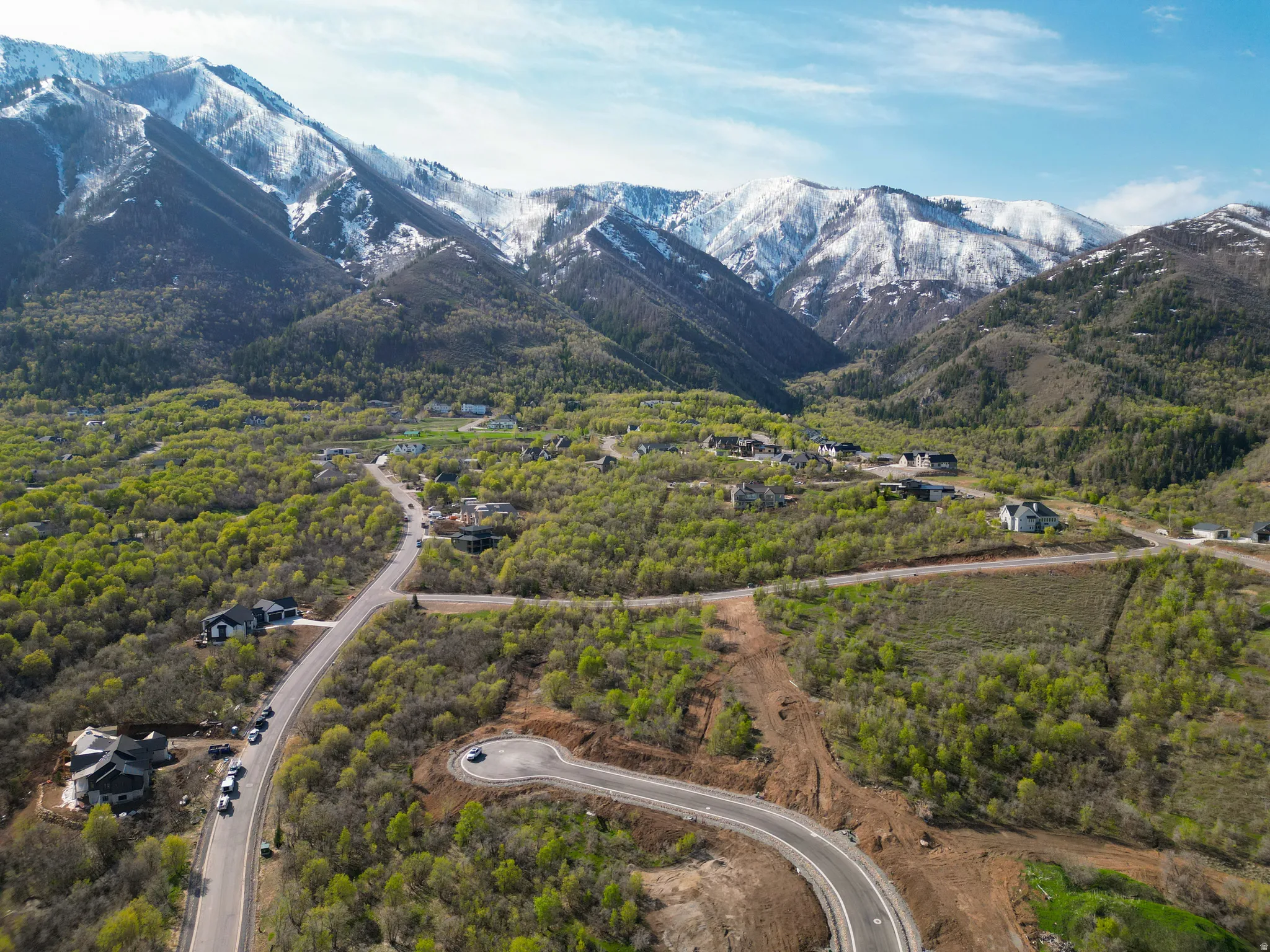 Aerial depiction of a development site featuring paved roads, scattered modern homes, and a mountainous backdrop with snow-capped peaks