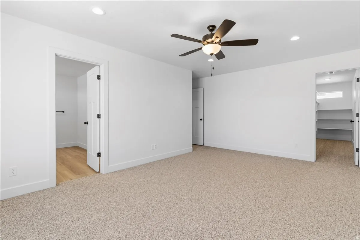 Spacious room featuring neutral carpeting, a ceiling fan with integrated lighting, recessed ceiling lights, and two doorways leading to additional areas