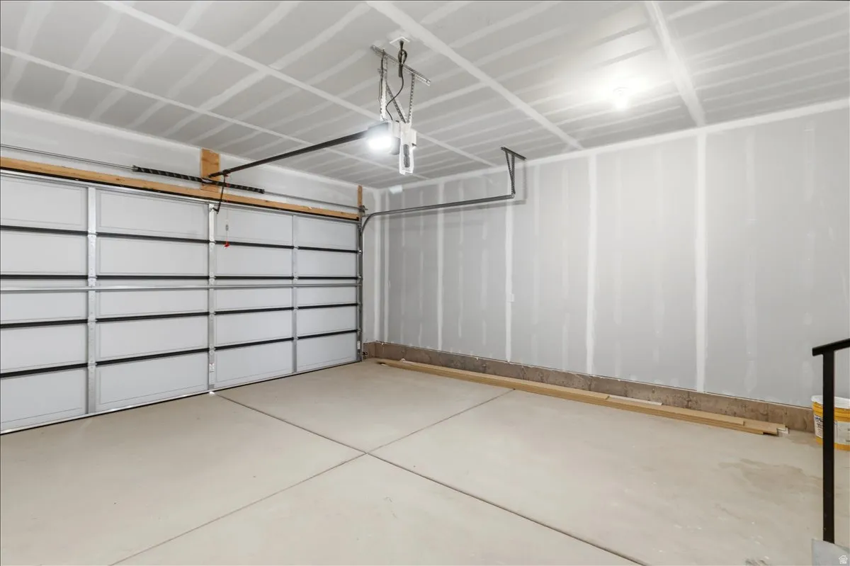 Attached two-car garage featuring a sectional overhead door, automatic opener, concrete flooring, and exposed drywall