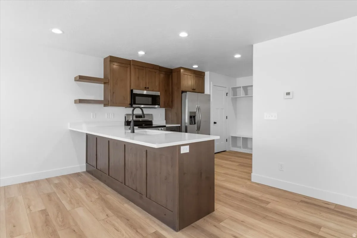 Kitchen featuring a central island with white countertop, wood-finish flooring, recessed lighting, stainless steel appliances, and wood cabinetry