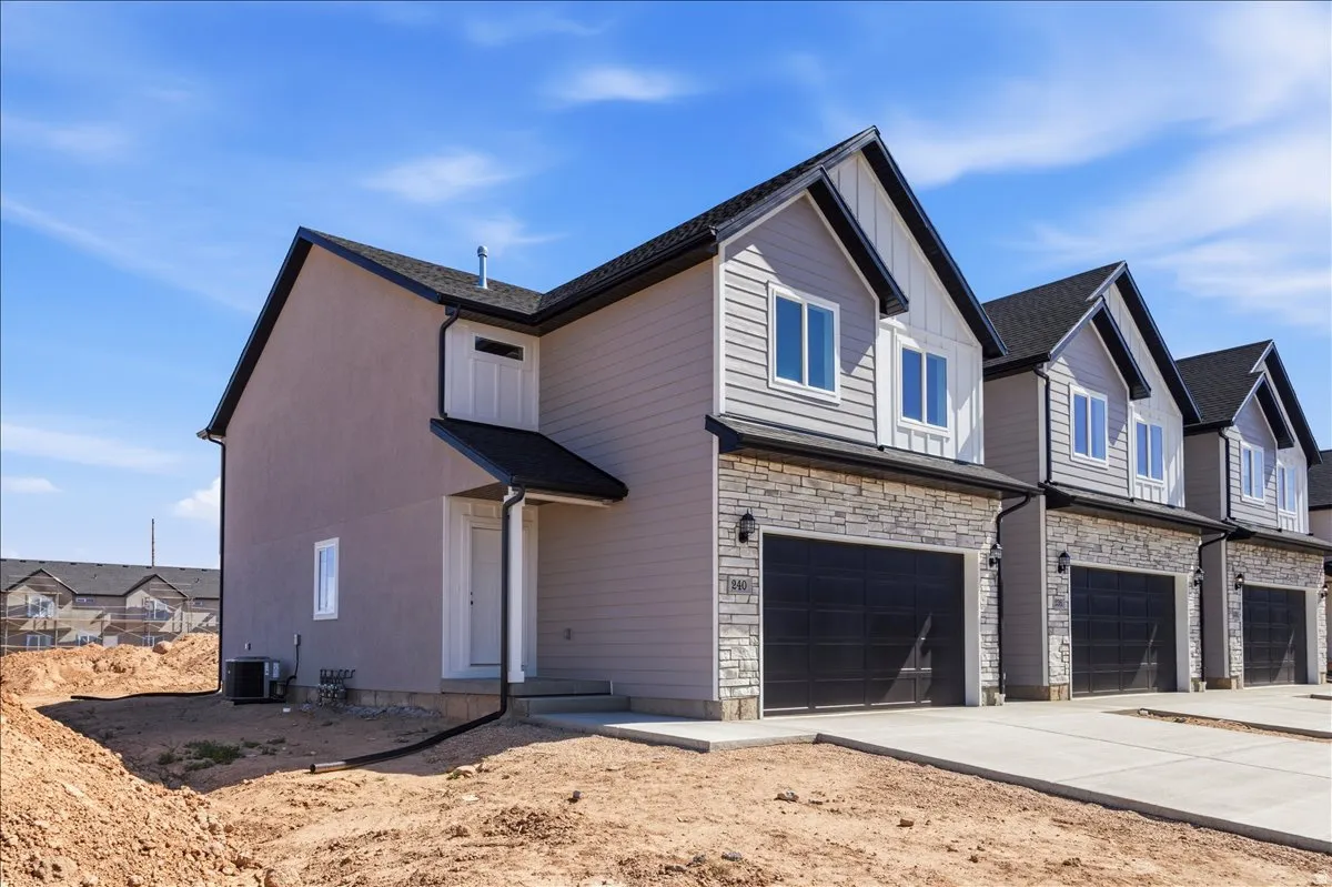 Contemporary townhome featuring a stone and siding exterior, black garage doors, and a covered entry