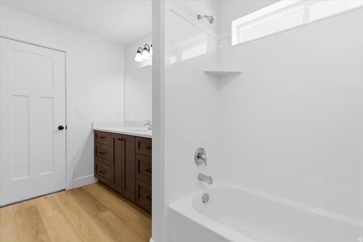 Bathroom featuring a white tub, wood-finish flooring, a wood-finish vanity with a light-colored countertop, and a translucent transom window