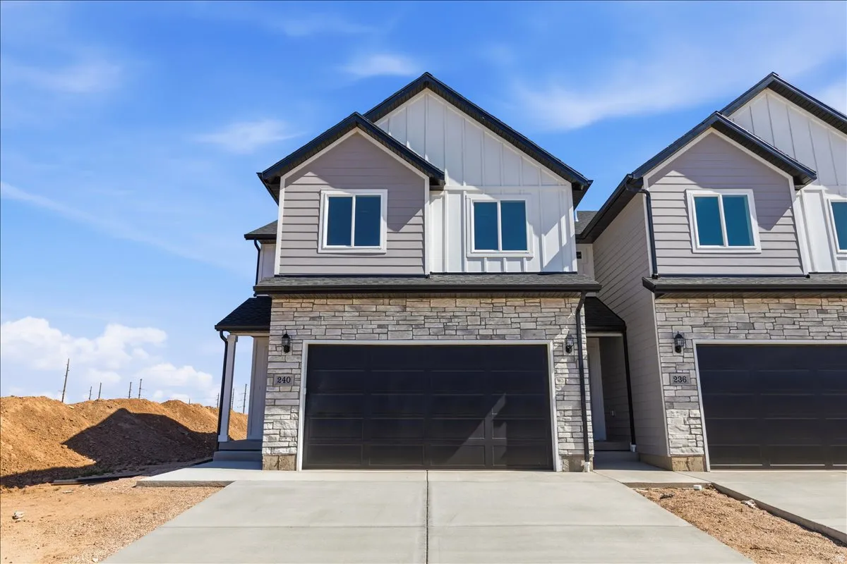 Two-story residence featuring a stone veneer and siding facade, black garage door, and a concrete driveway