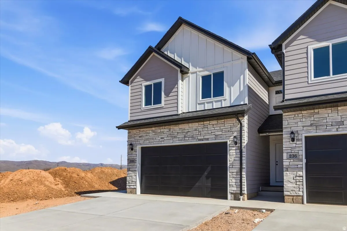 Contemporary townhome exterior featuring multi-toned siding, stacked stone accents, a dark garage door, and modern exterior lighting fixtures