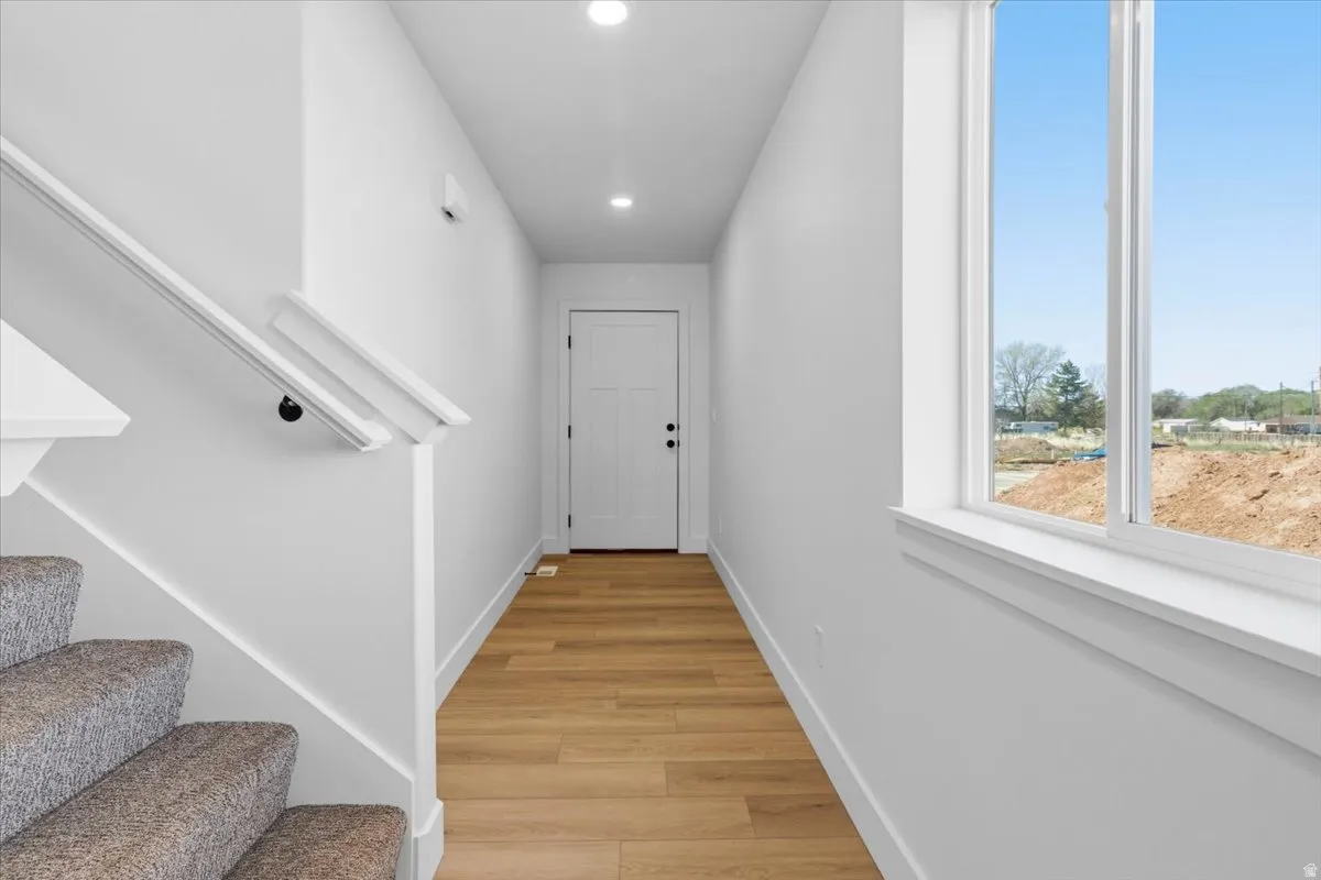 Foyer featuring wood-finish flooring, recessed lighting, white walls, a staircase with carpeted treads and a white handrail, and a large window