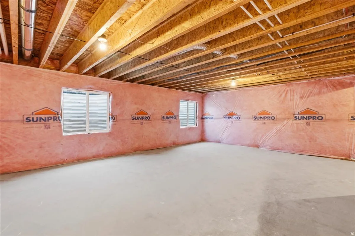 Unfinished basement space featuring exposed wood joists, insulated walls, concrete flooring, and two visible windows