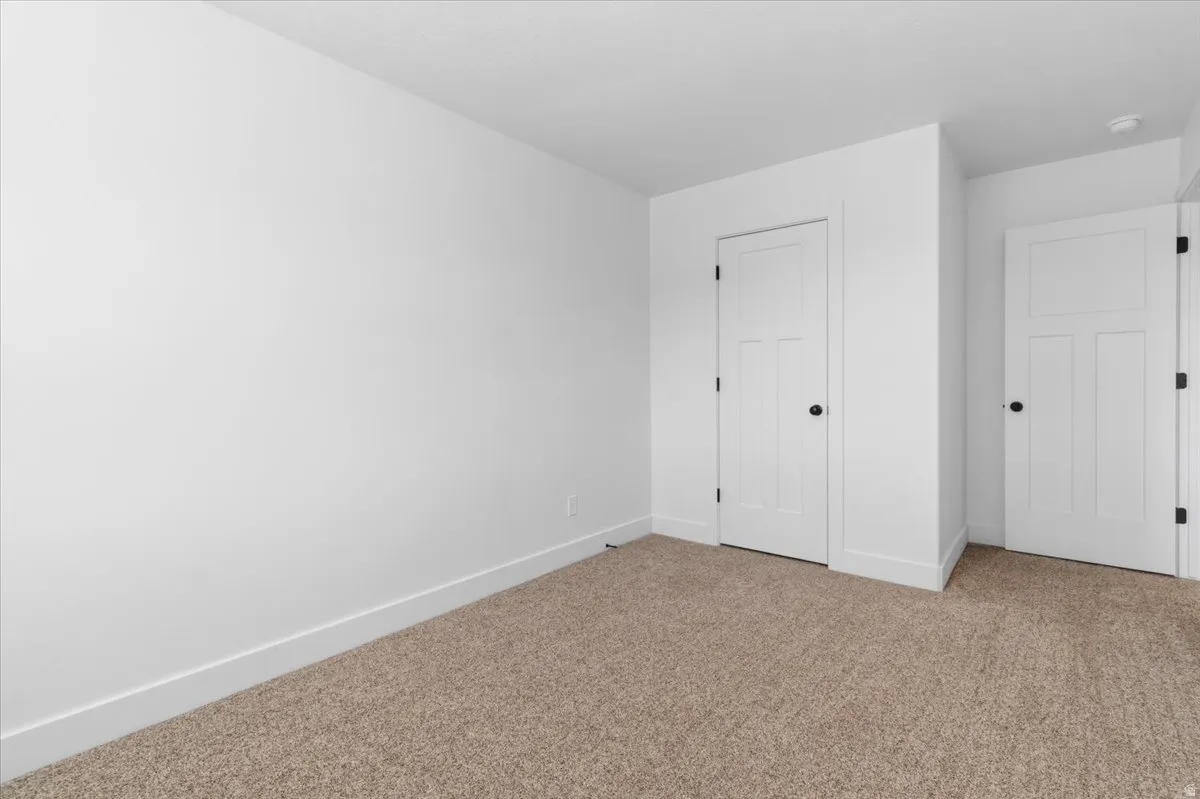 Neutral wall color, plush carpet flooring, white trim, and two paneled doors with matte black hardware