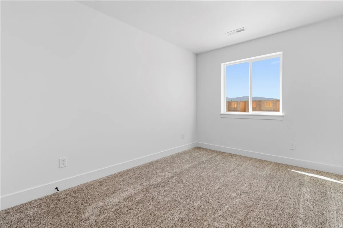 Light-filled room featuring a broad window, neutral-toned carpet, white walls, and bright baseboards