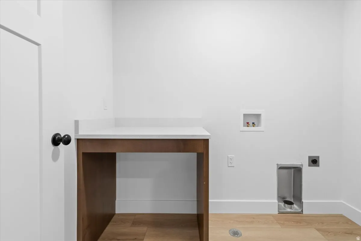 Laundry area featuring wood-finish flooring, white walls, and a built-in wood-tone countertop with a light-colored surface