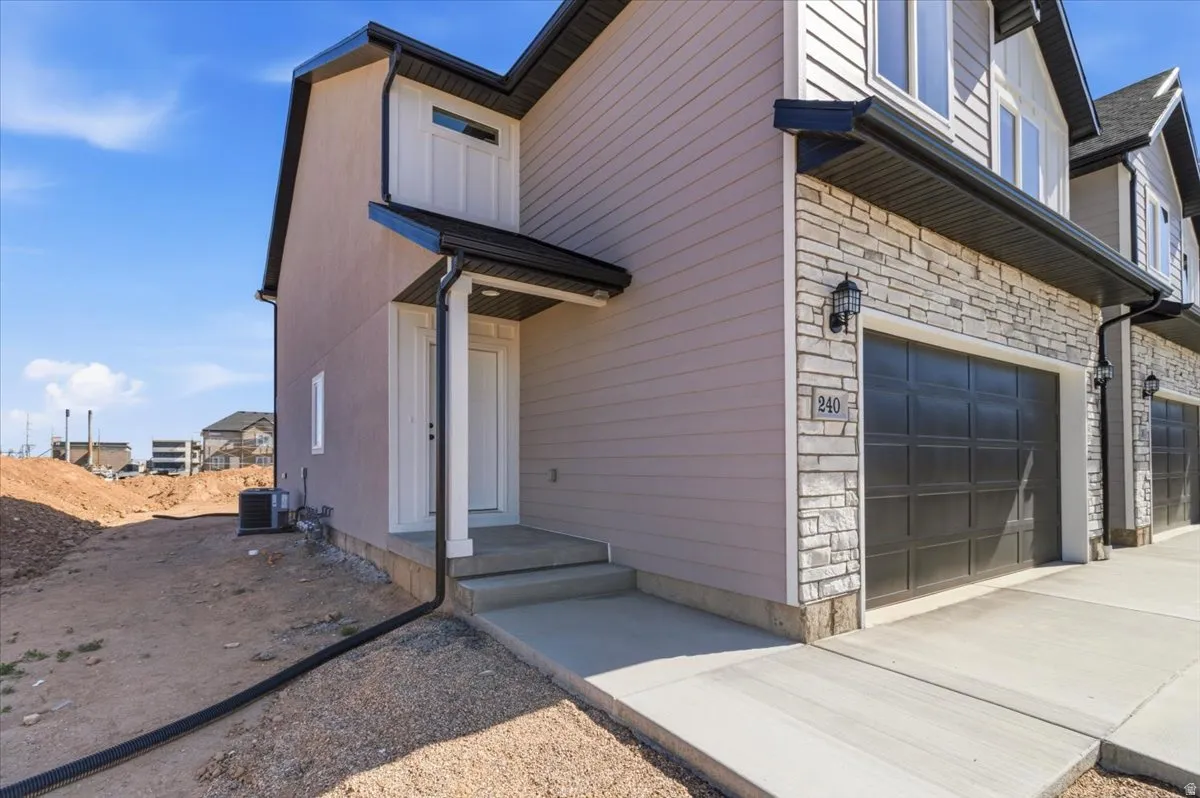 Multi-level exterior featuring light-toned siding, stacked stone accents, and a dark paneled garage door