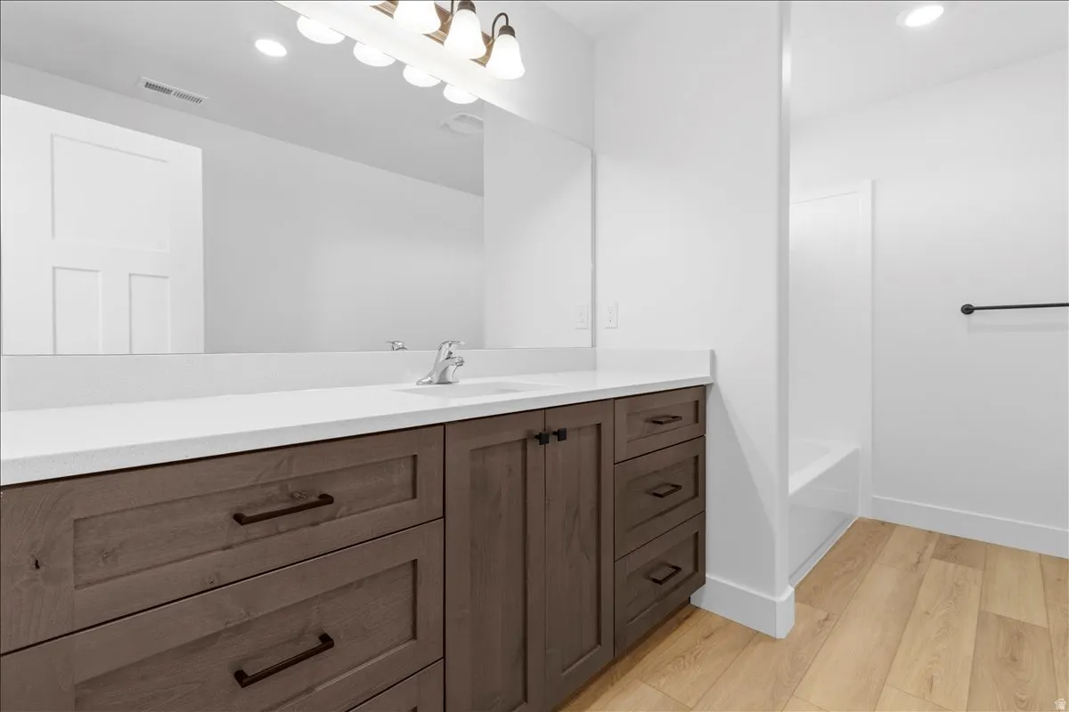 Bathroom featuring a long vanity with wood-finish cabinetry, solid surface countertop, and large wall mirror