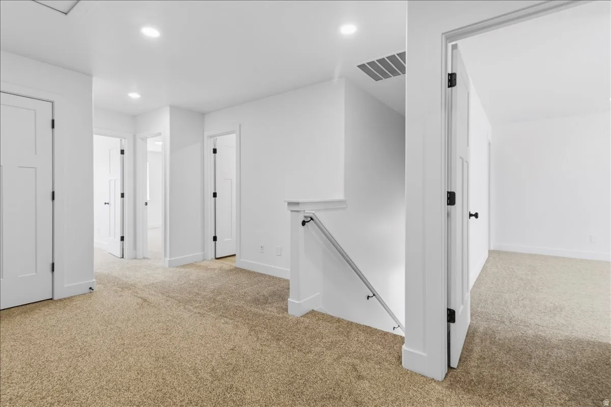 Carpeted landing featuring multiple white panel doors with black hardware, recessed lighting, and a staircase with a white railing and metal handrail