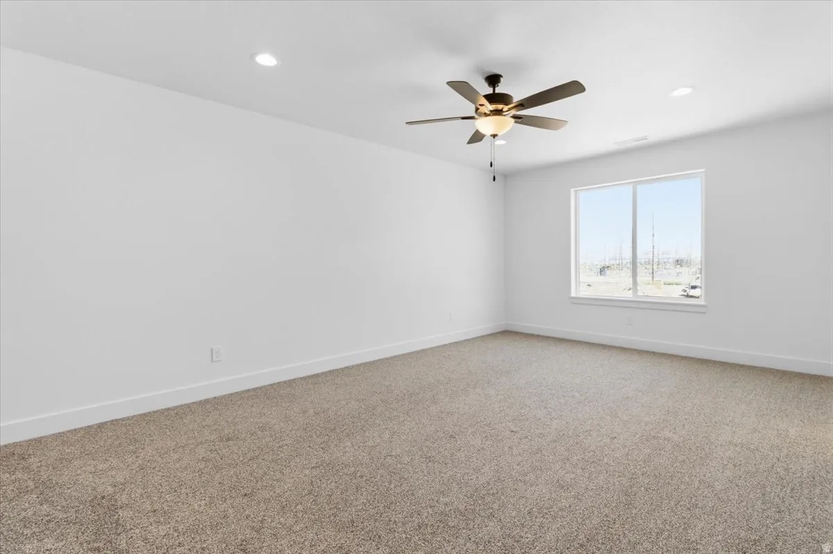 Spacious room featuring neutral carpeting, a large window, a ceiling fan with integrated lighting, and recessed ceiling lights