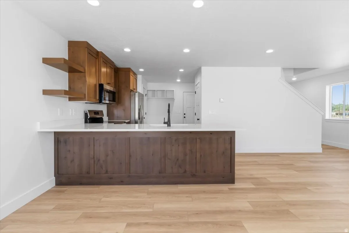 Modern kitchen featuring light wood-finish flooring, white walls, recessed lighting, and a kitchen island with a dark wood-finish base and light-colored countertop