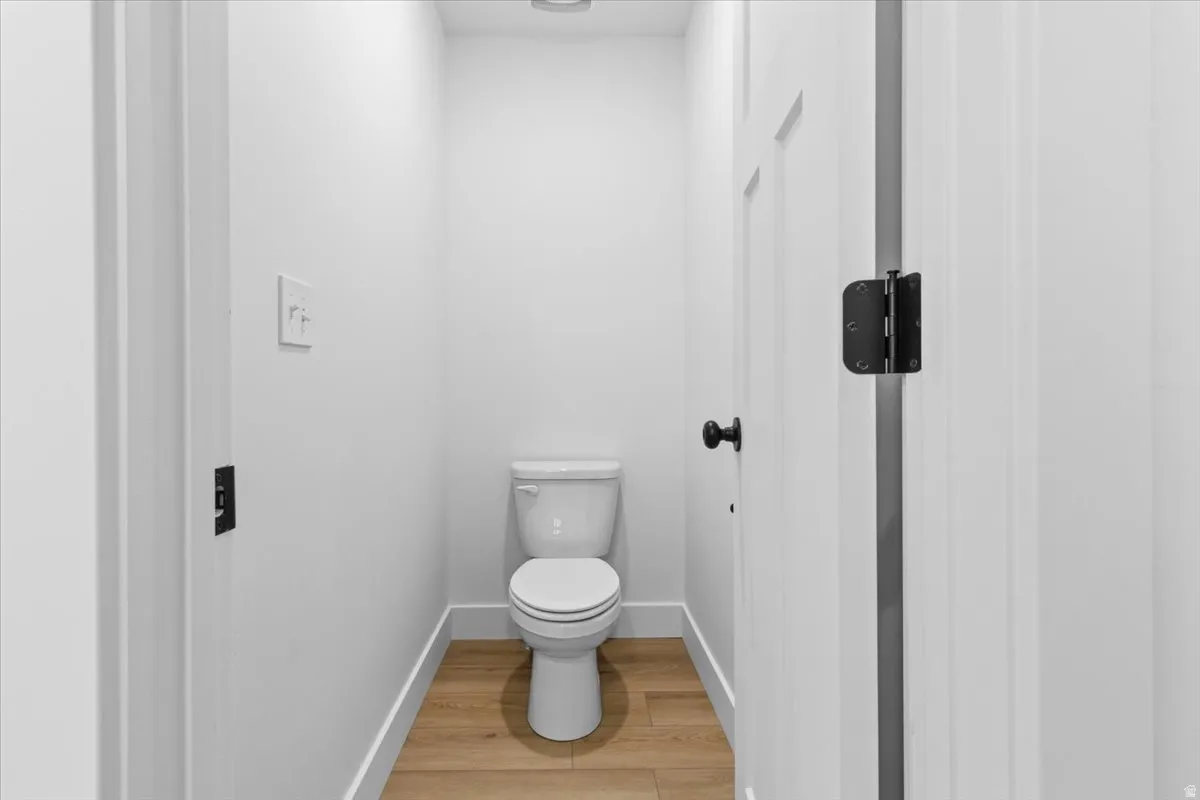 Powder room featuring a two-piece toilet, wood-finish flooring, white baseboards, and a contemporary light switch