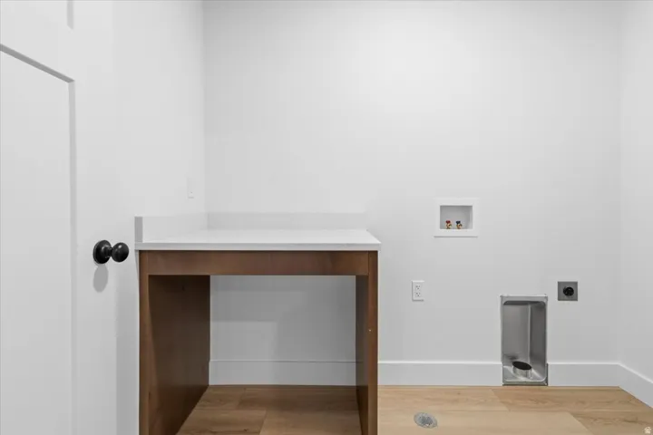 Laundry area featuring wood-finish flooring, white walls, and a built-in wood-tone countertop with a light-colored surface