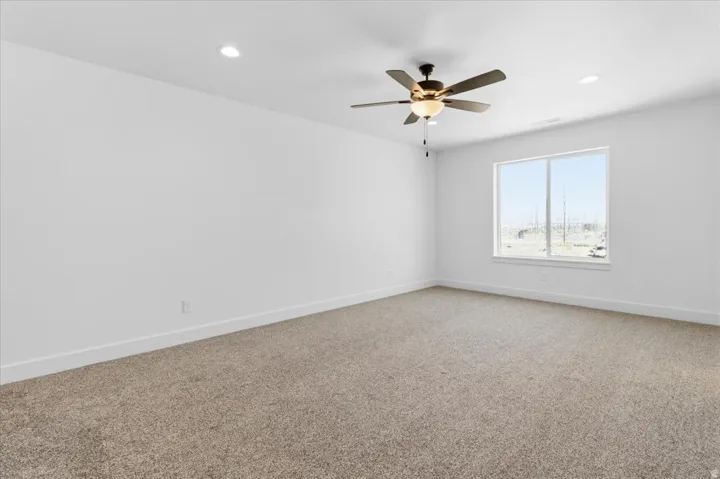 Spacious room featuring neutral carpeting, a large window, a ceiling fan with integrated lighting, and recessed ceiling lights