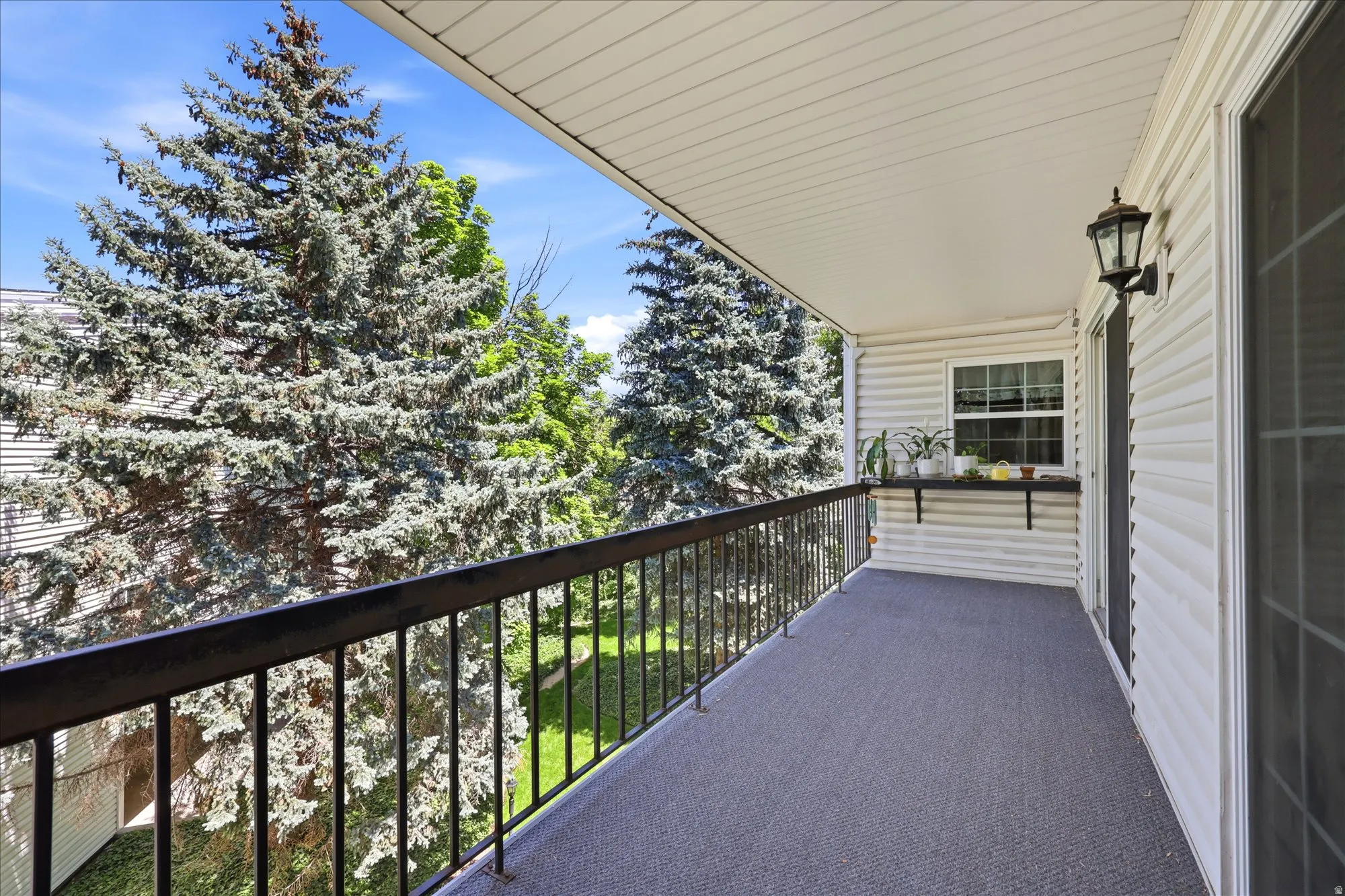 Covered balcony featuring a textured gray surface, wrought iron railing, and exterior wall lantern