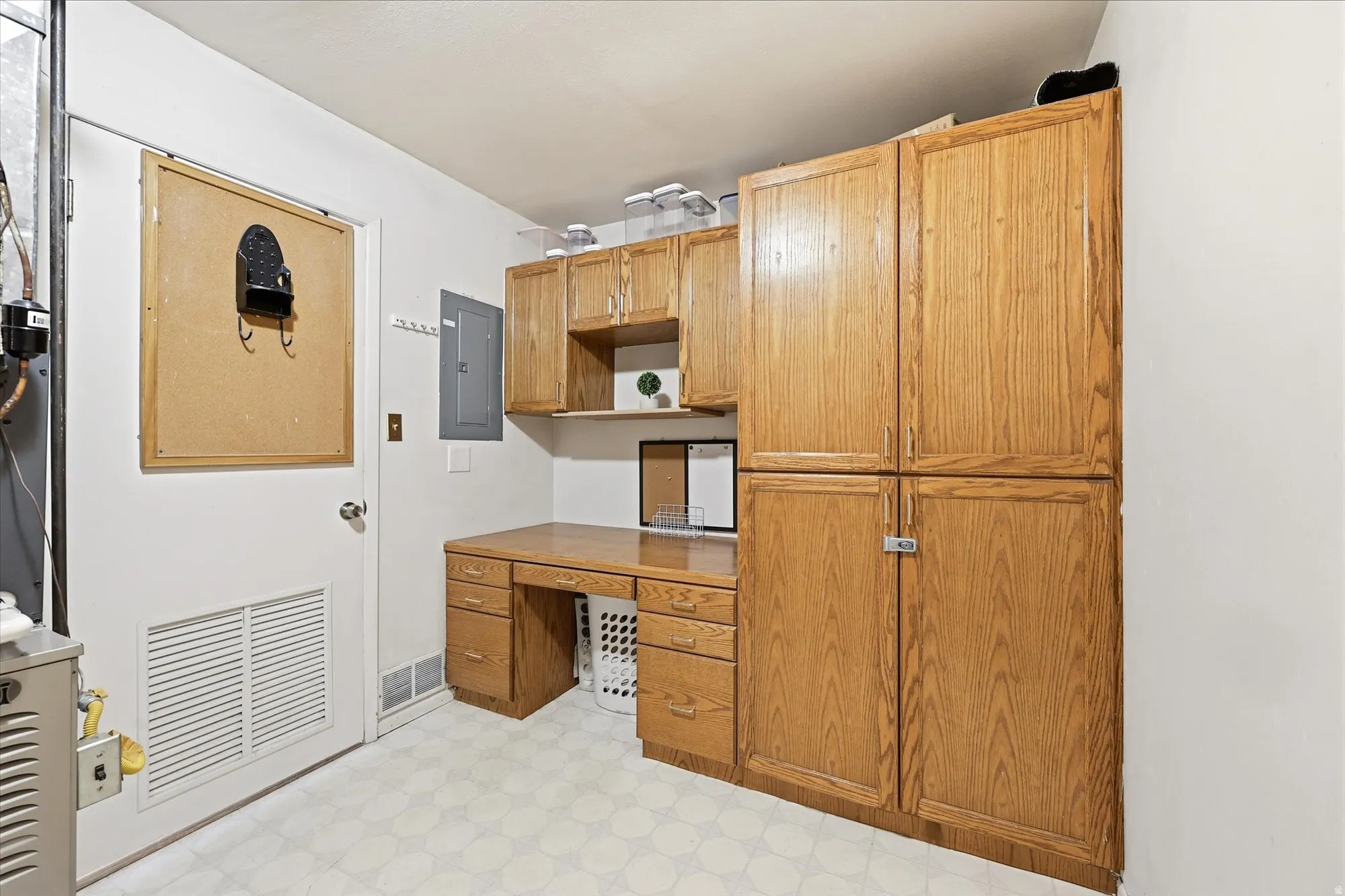 Laundry area featuring wood-finish cabinetry, built-in desk, patterned vinyl flooring, and overhead lighting
