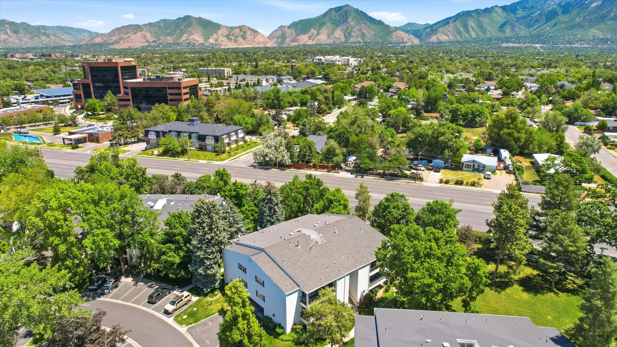 Aerial perspective showcasing a multi-story residential building with a gray roof and white exterior, surrounded by mature trees